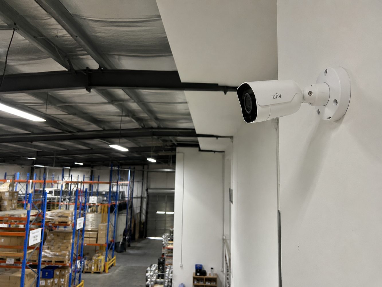 Bullet security camera installed on a warehouse wall overlooking inventory aisles